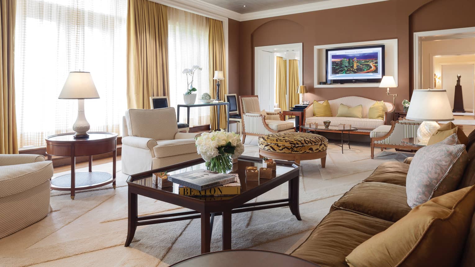 Presidential Suite living area coffee table with books and fresh white flowers, white armchair, tiger-print ottoman, sofas