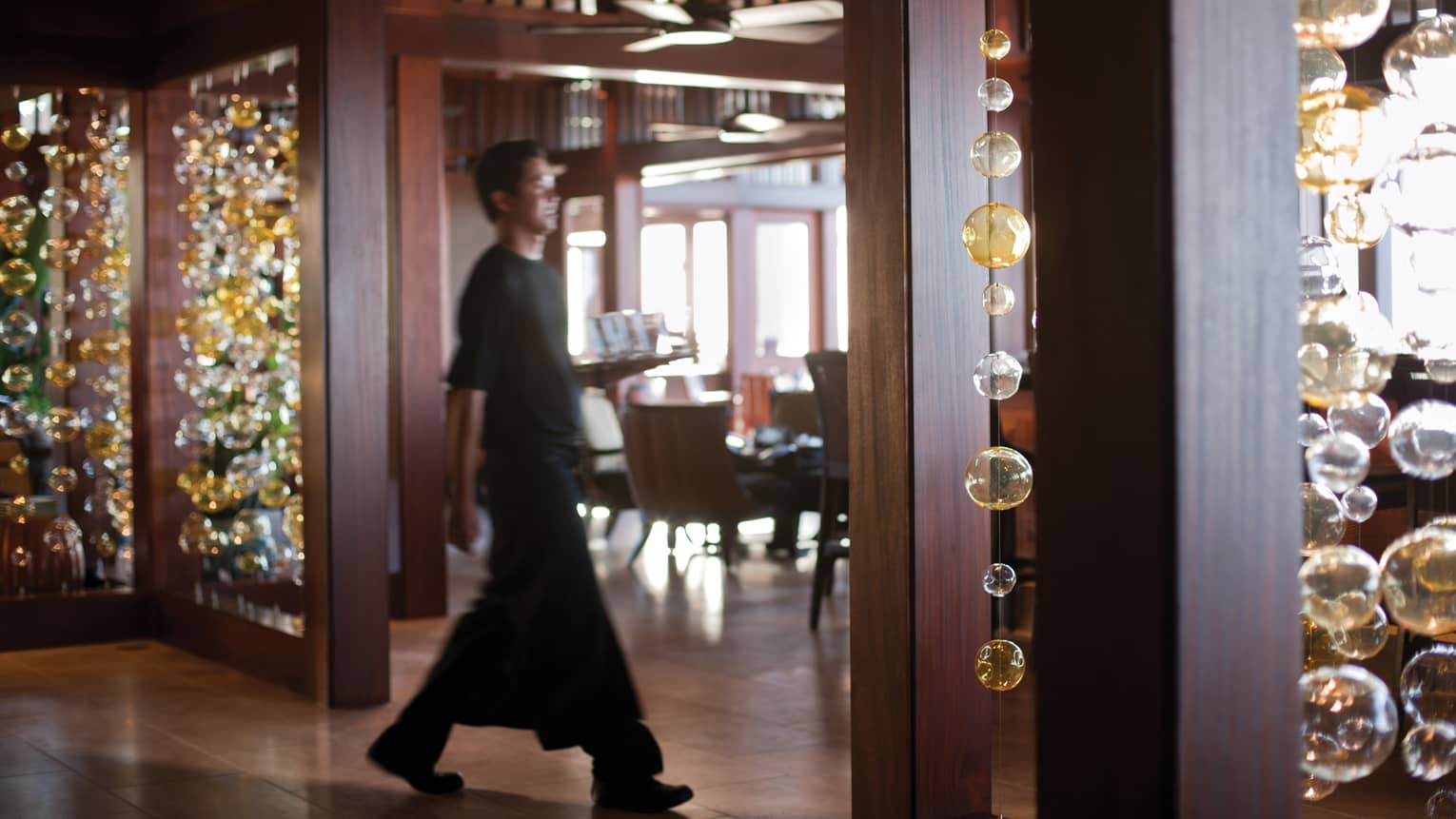 Server carries tray through ULU Sushi Lounge, past long glass bulb strings