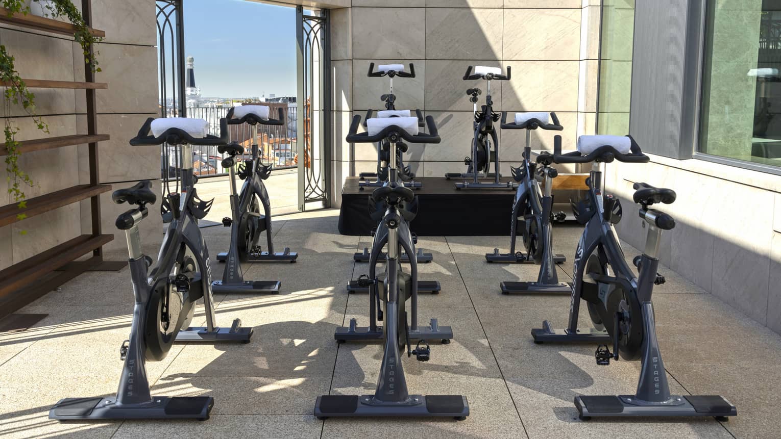 A partially walled outdoor workout space outfitted with stationary bikes, with city views in the background