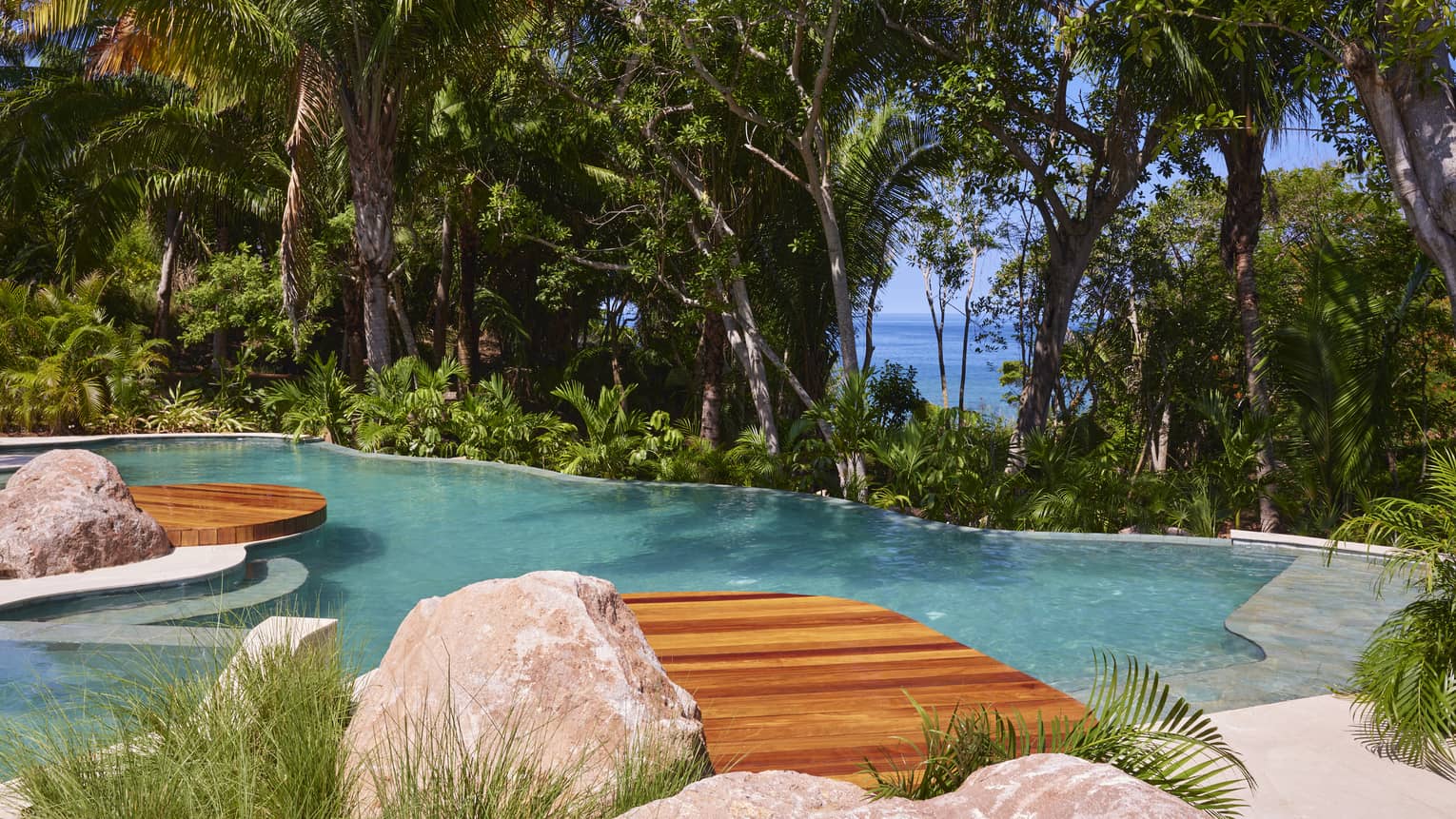 Pool surrounded by tropical forest, with the ocean visible through the trees