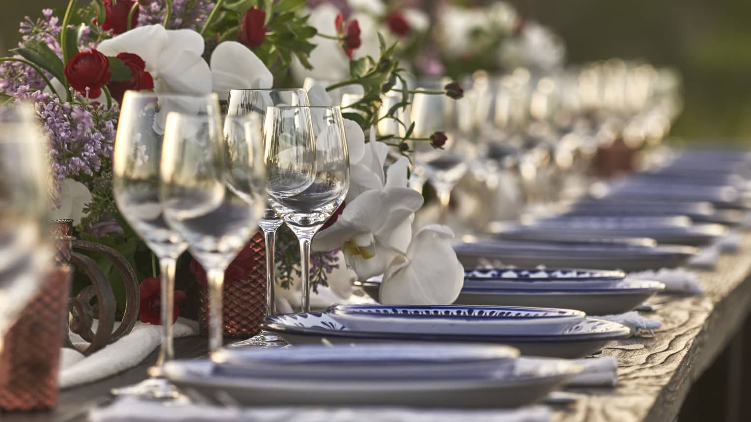 Table setting with wine glasses, plates and flowers on long dining table