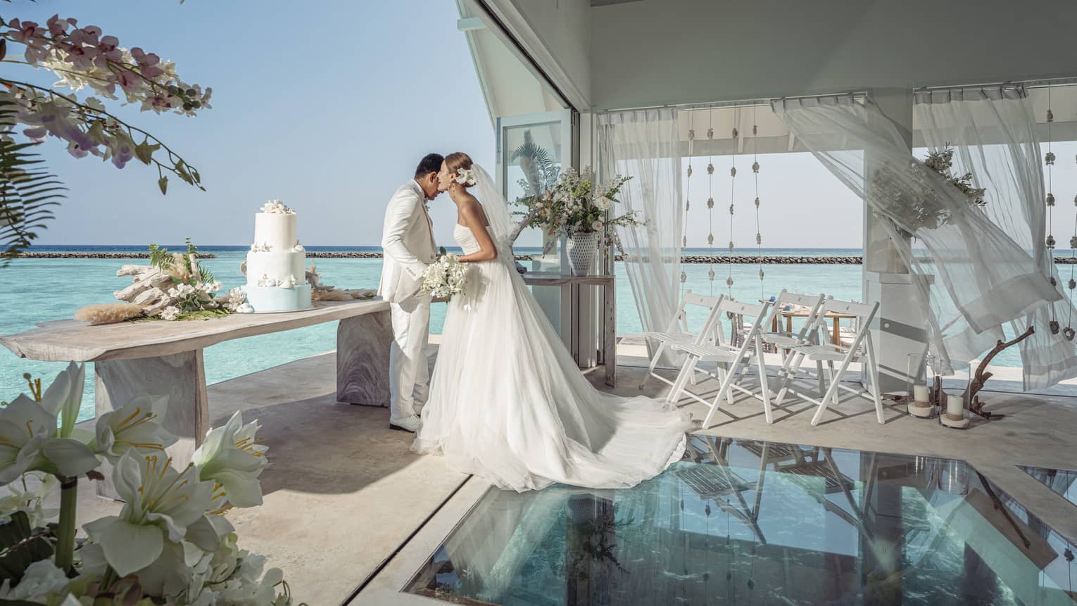 Bride whispers in groom?s ear in the glass-bottom overwater wedding pavilion