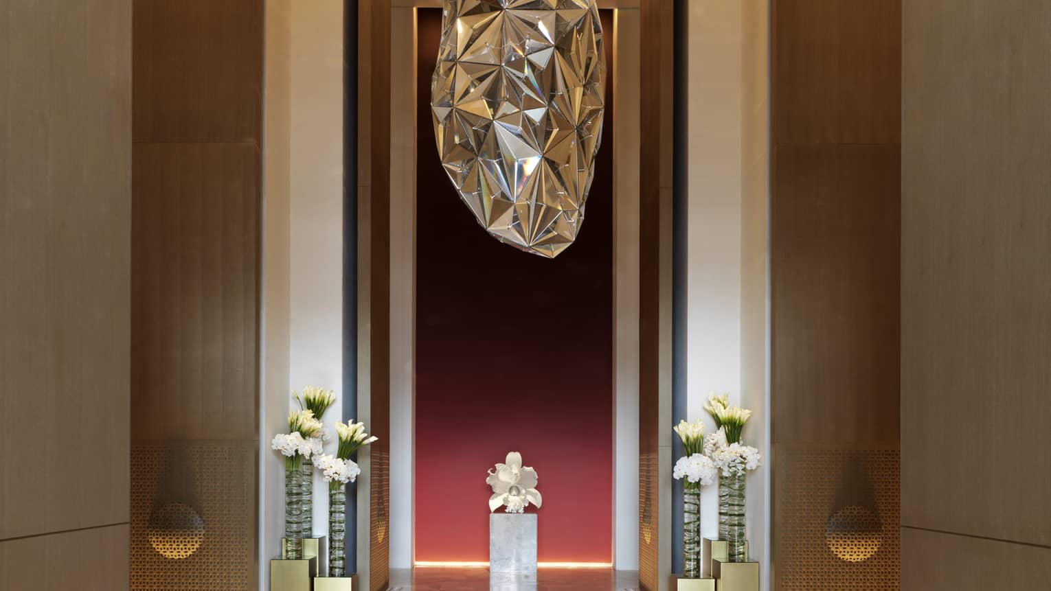 Large silver sculpture hanging above marble floors, tall vases with fresh white flowers