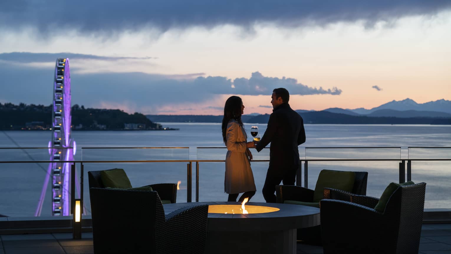 A couple holds hands and shares wine on the balcony as the sun sets