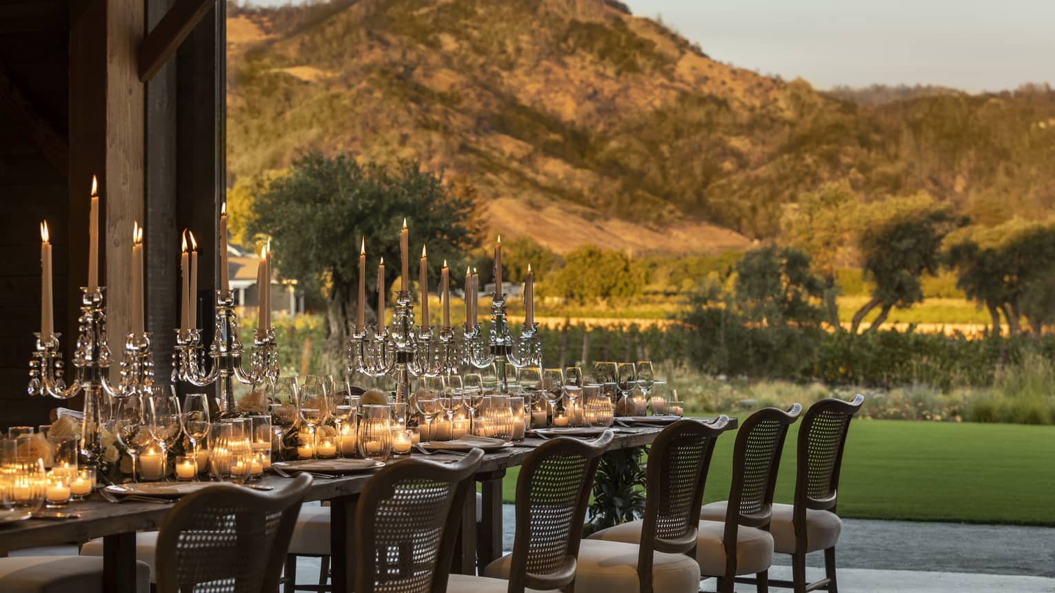 A long table with candles outside near mountains.