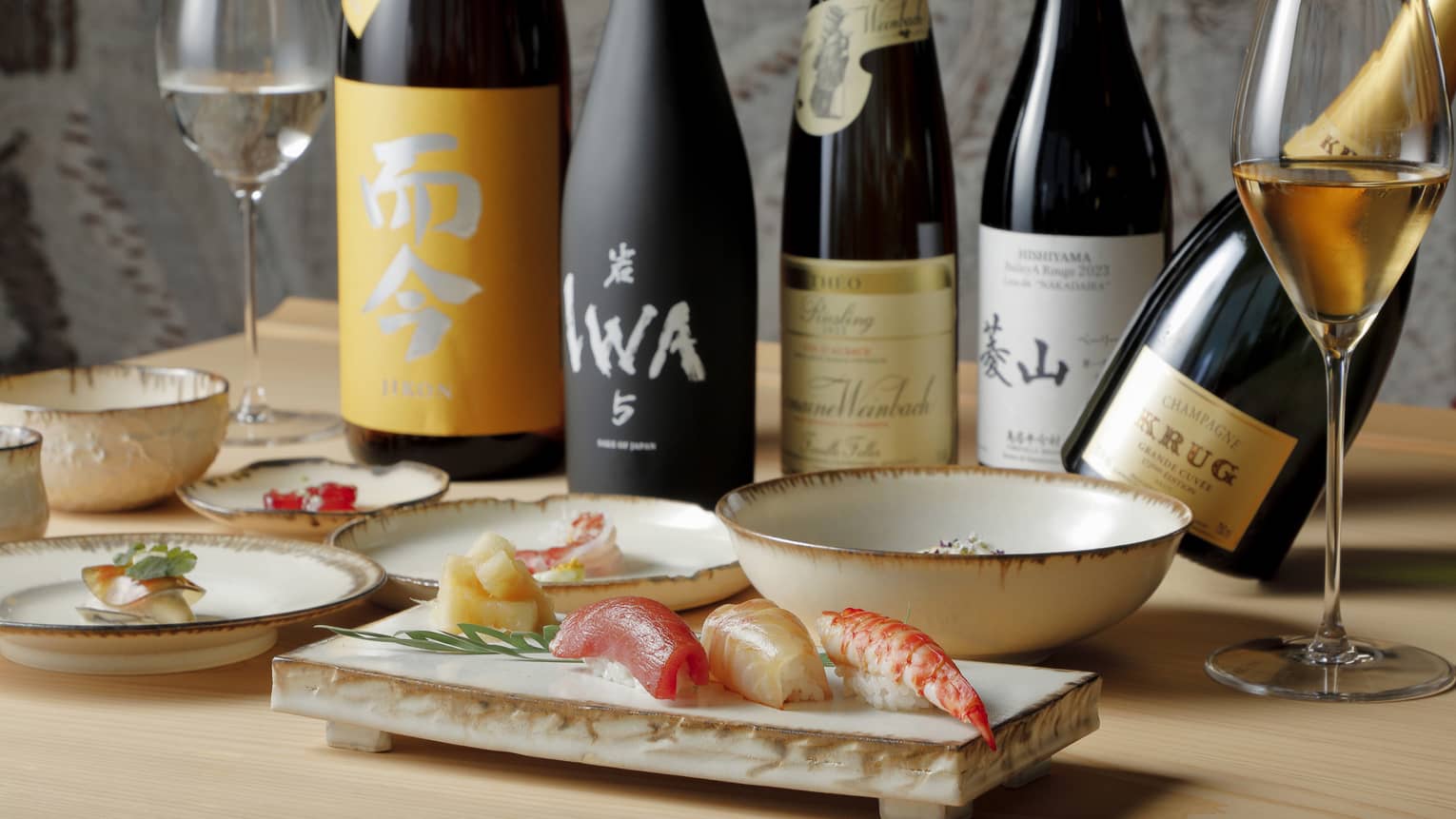 Bottles of sake and Krug champagne and glasses of wine behind dishes artfully laden with vibrant sushi and other delicacies.
