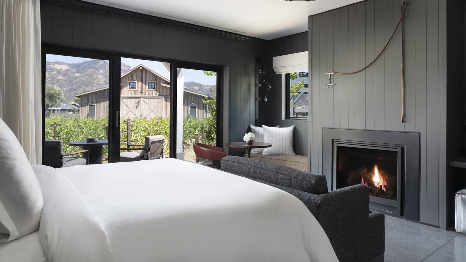 Luxury resort room with a king bed, cozy fireplace, vineyard view, seating area and outdoor patio facing rustic barn and mountains