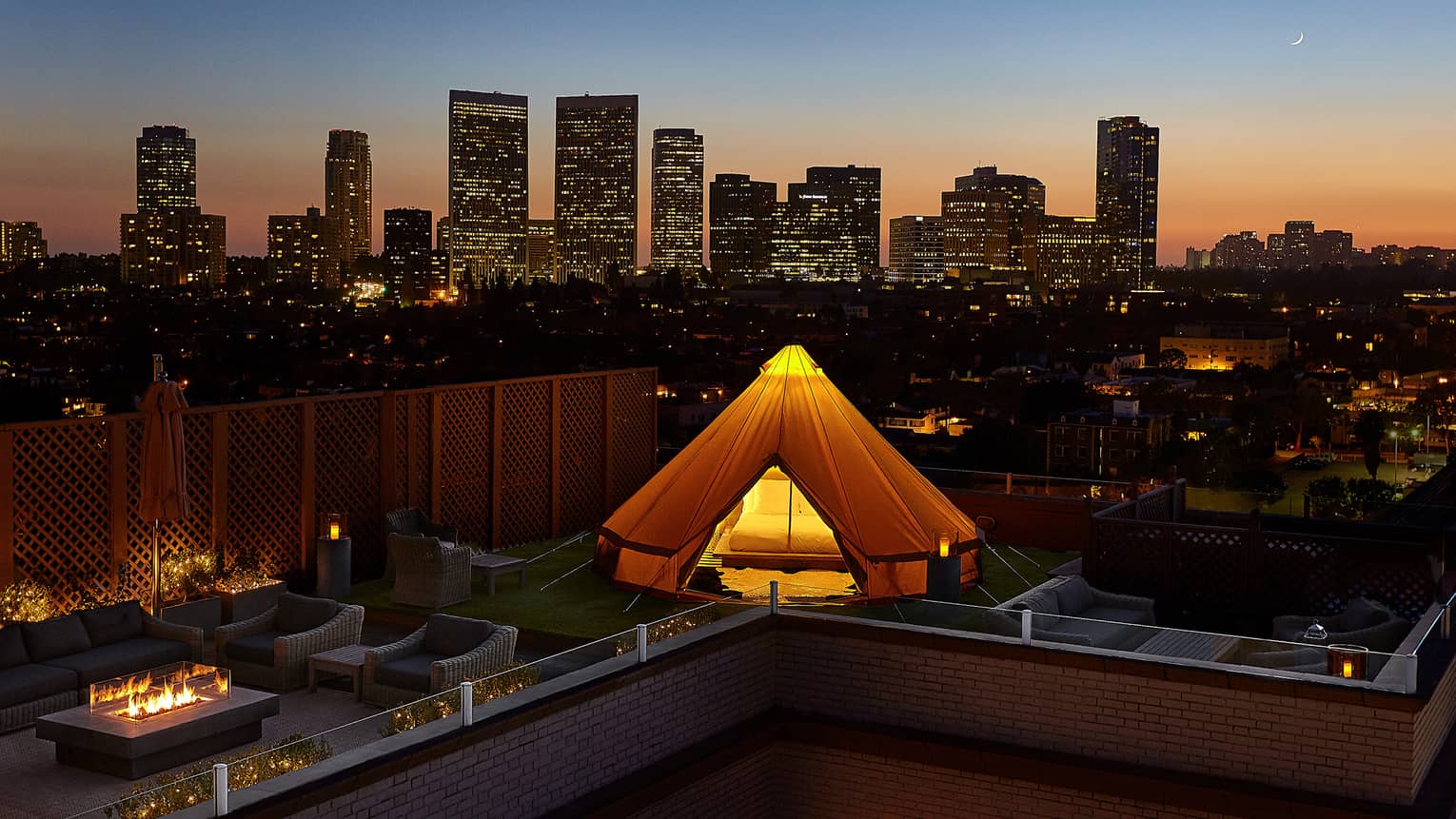 Glowing white tent, bed on rooftop patio by chairs, outdoor fireplace, Beverly Hills sunset city views