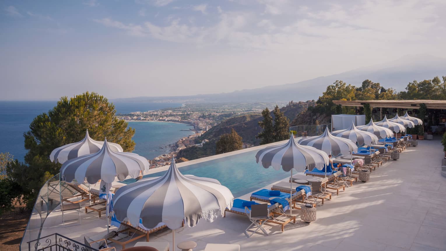 Long rectangular infinity pool with playful striped umbrellas, view of coastline