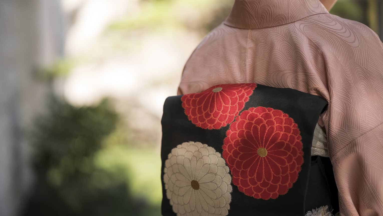 Back view of a person wearing a pink kimono with a black obi featuring red and white floral designs