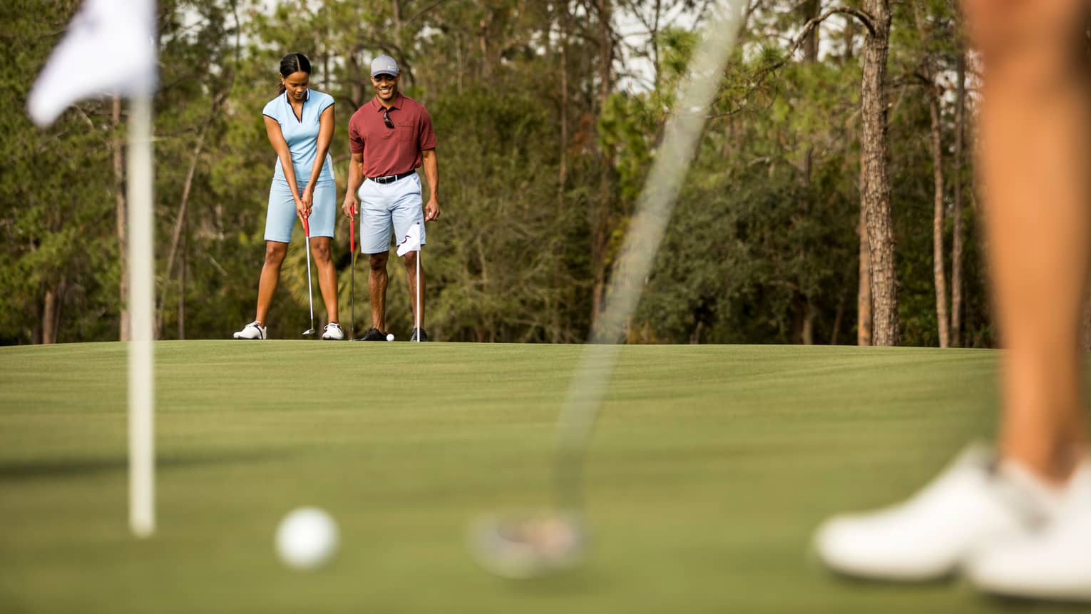 View past golfer to smiling couple preparing to putt on golf course