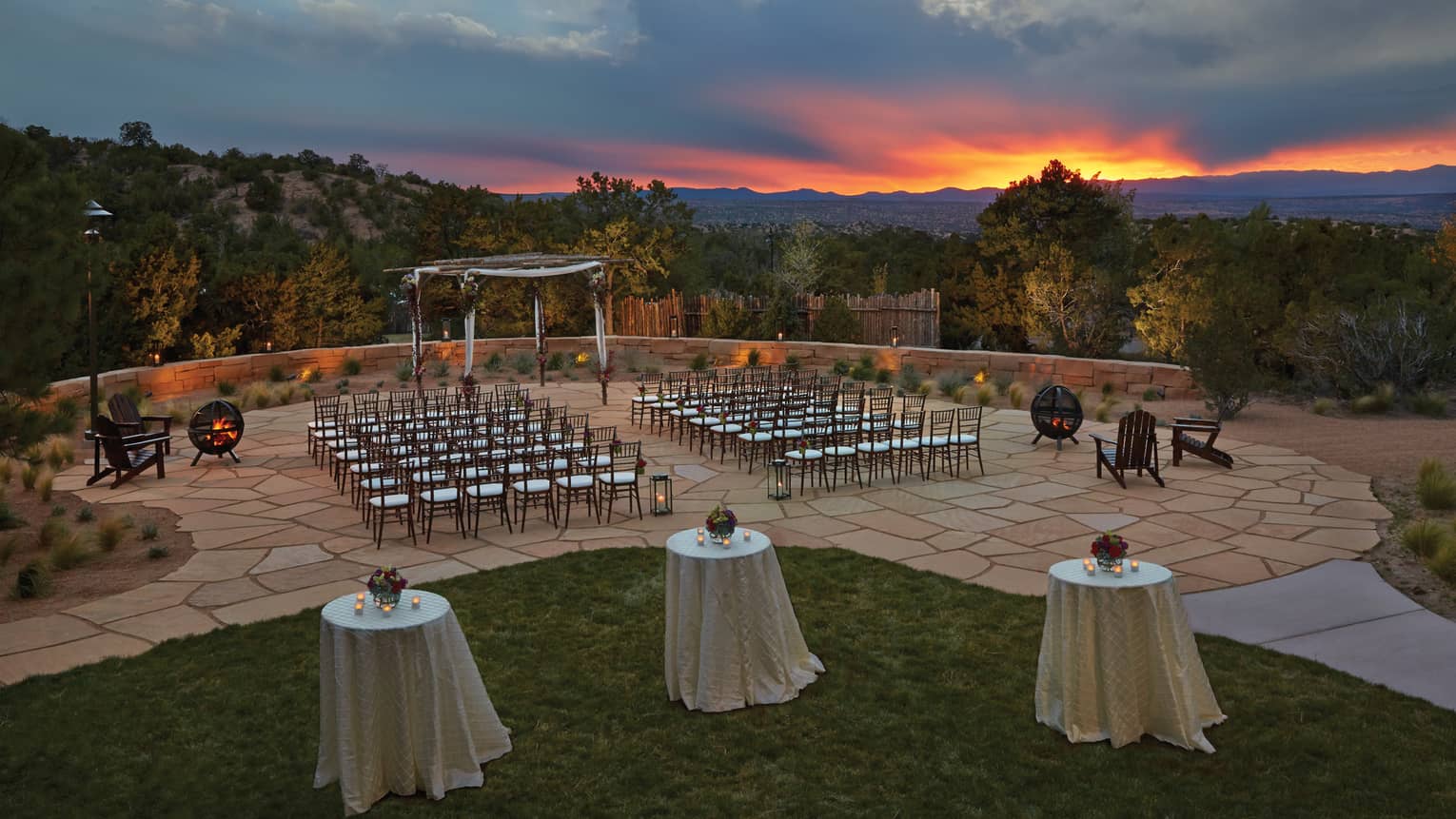 Rows of chairs on tiled surface facing wooden altar, cocktail tables overlooking trees and foothills at dusk