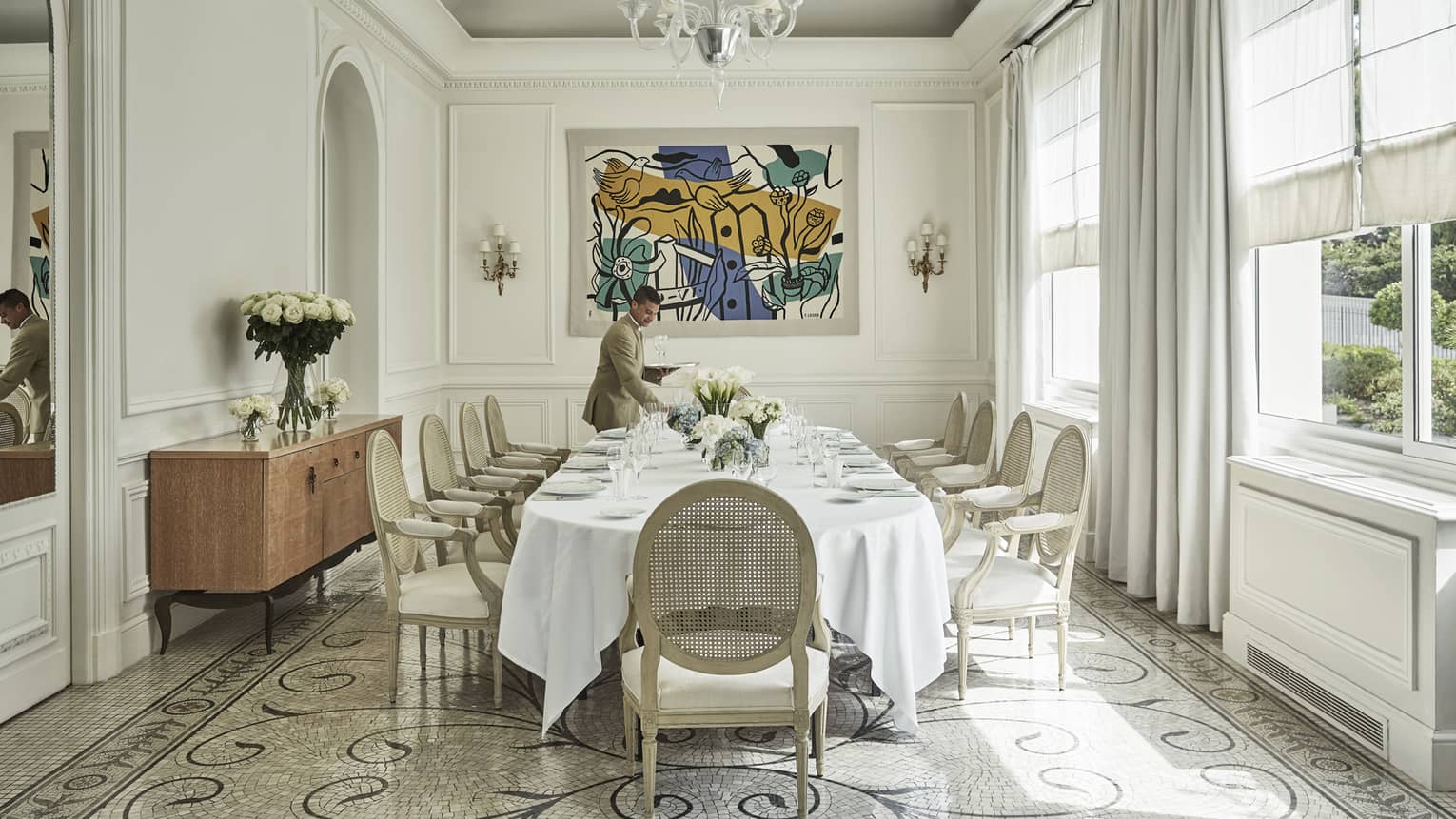 Server sets table in bright Salon les pins event space with modern art, tile floors, large windows