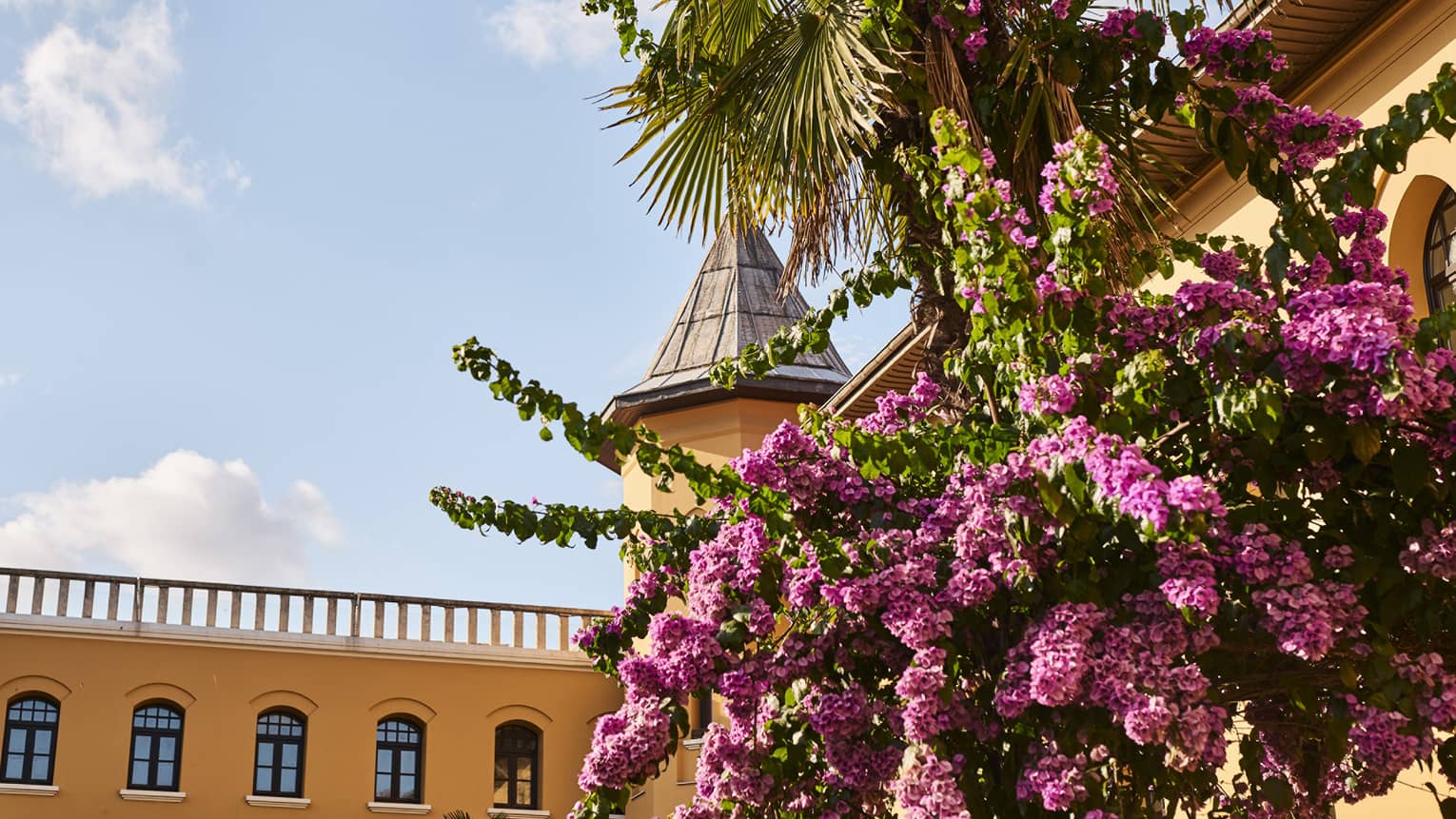 Exterior of yellow hotel's top floor and turret with fuchsia flowers cascading