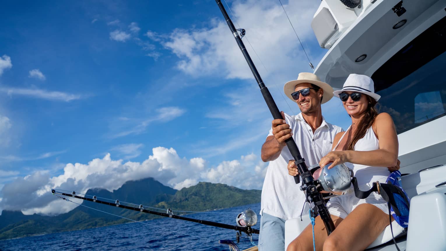 Smiling couple in sun hats fishes from yacht