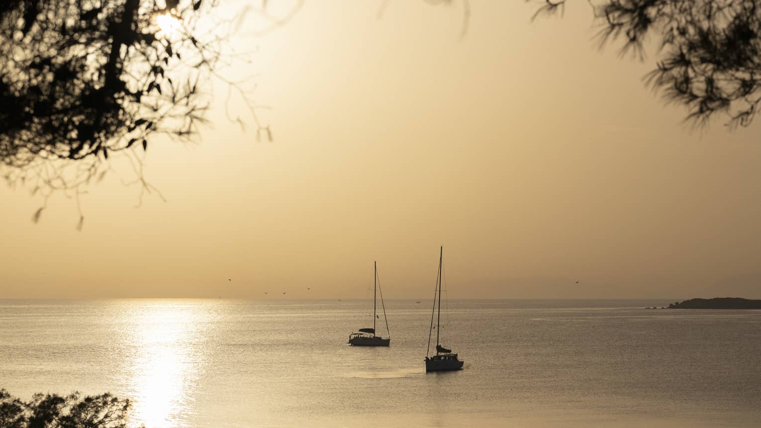 Silhouette of two sailboats at dusk on ocean cruising Greek isles. 
