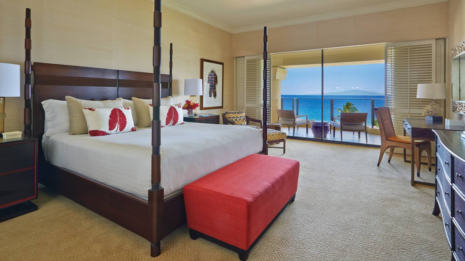 Luxury bedroom with a four-poster bed, red bench and balcony offering ocean view at a tropical resort suite