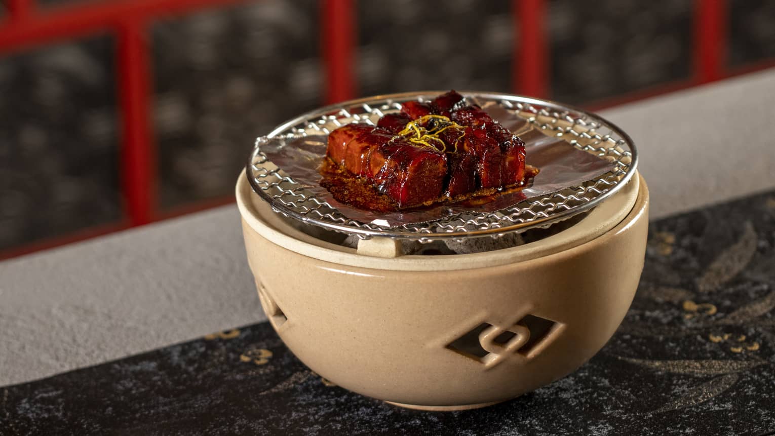 Barbecued pork on piece of foil atop tan clay bowl with cutouts