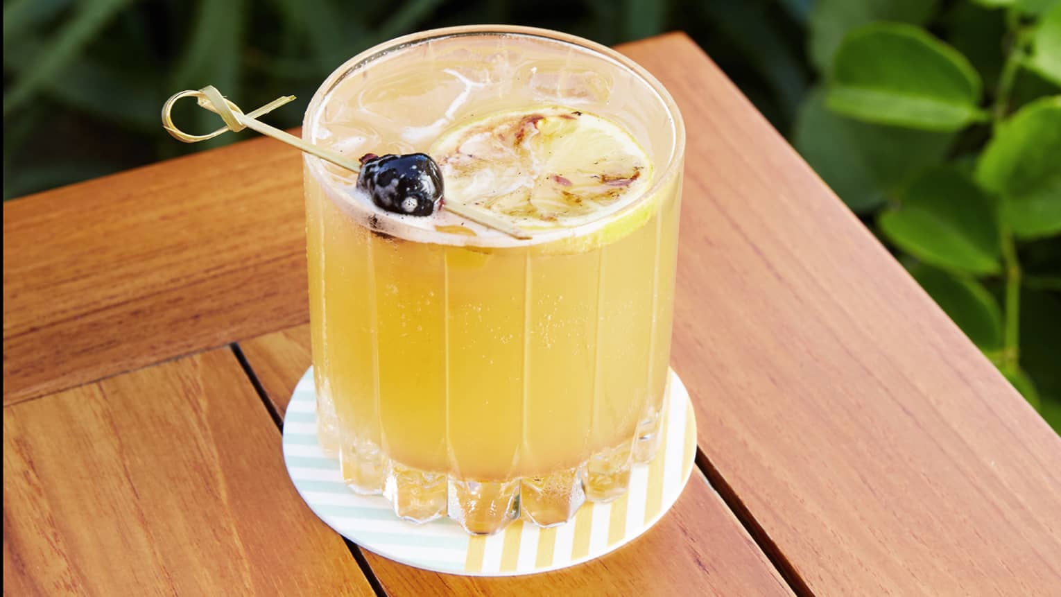 Yellow drink in a glass on a coaster on an outdoor table.