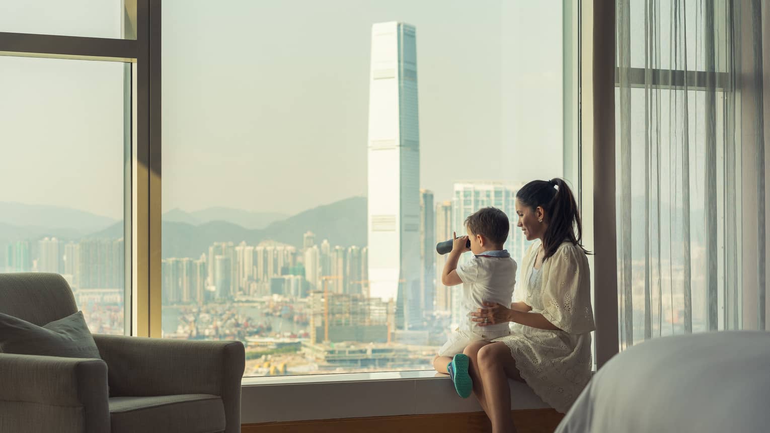 A mother and child are looking out at the city through binoculars