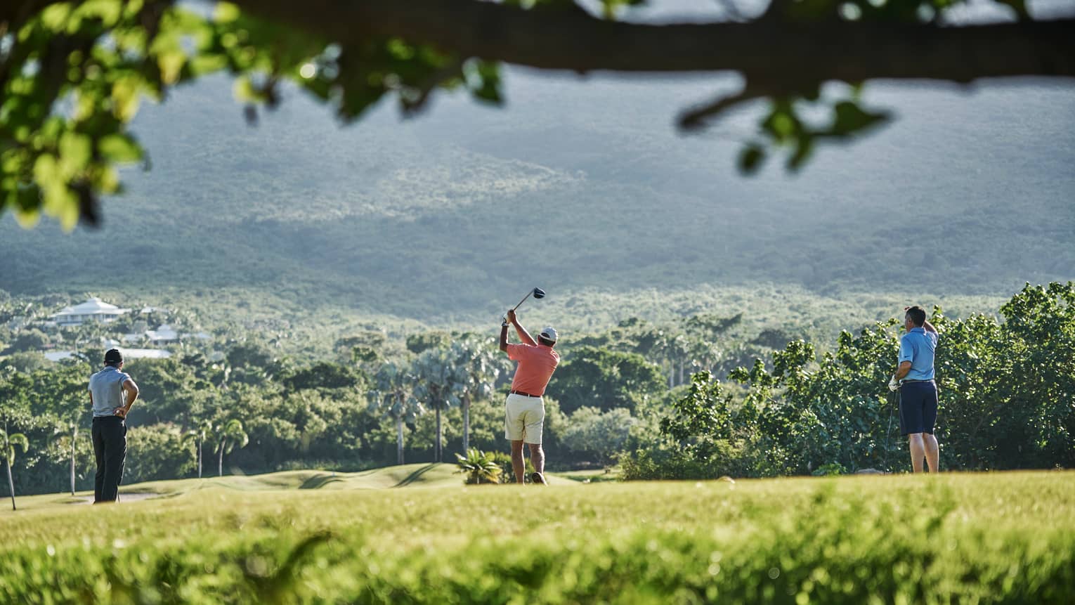 Back of three people standing on Robert Trent Jones II Golf Course, man swings golf club