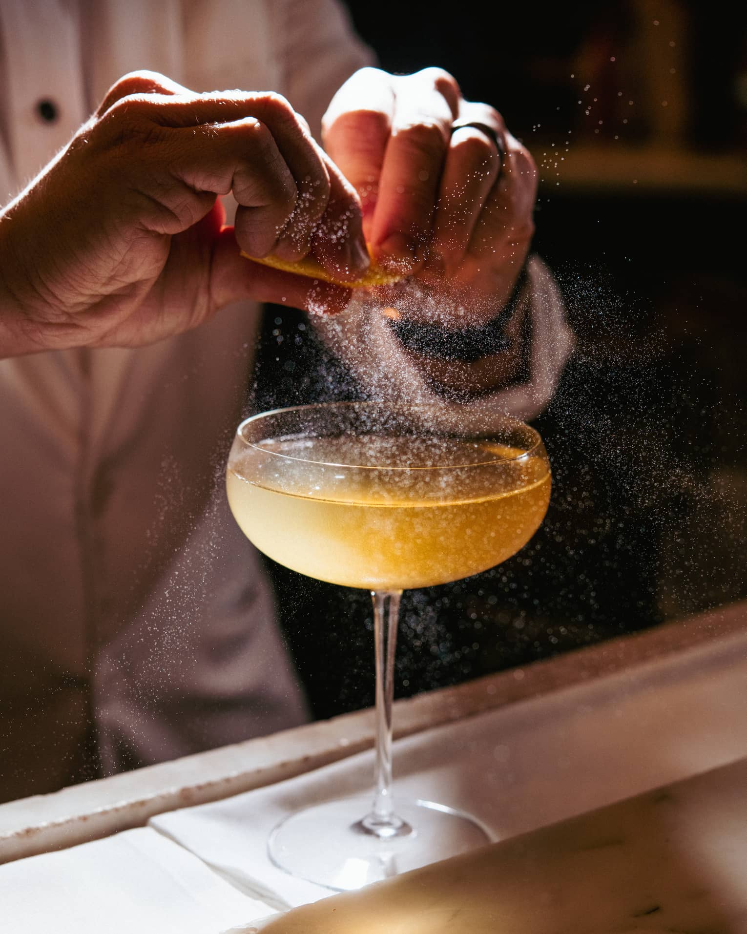 A cocktail being garnished with an orange spritz.