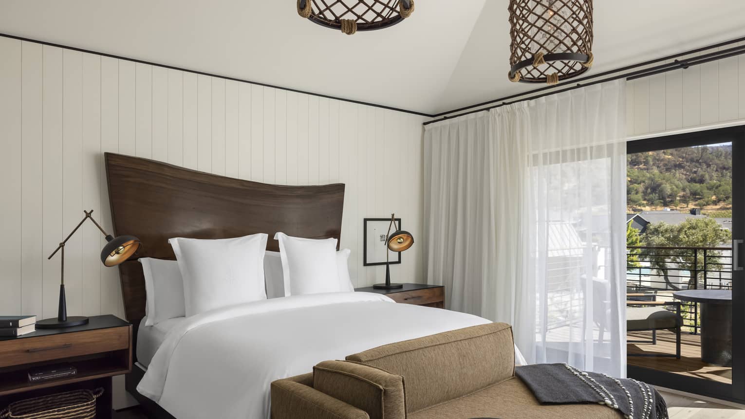 Bedroom with natural wood headboard and white king bed, brown chaise, walk-out terrace