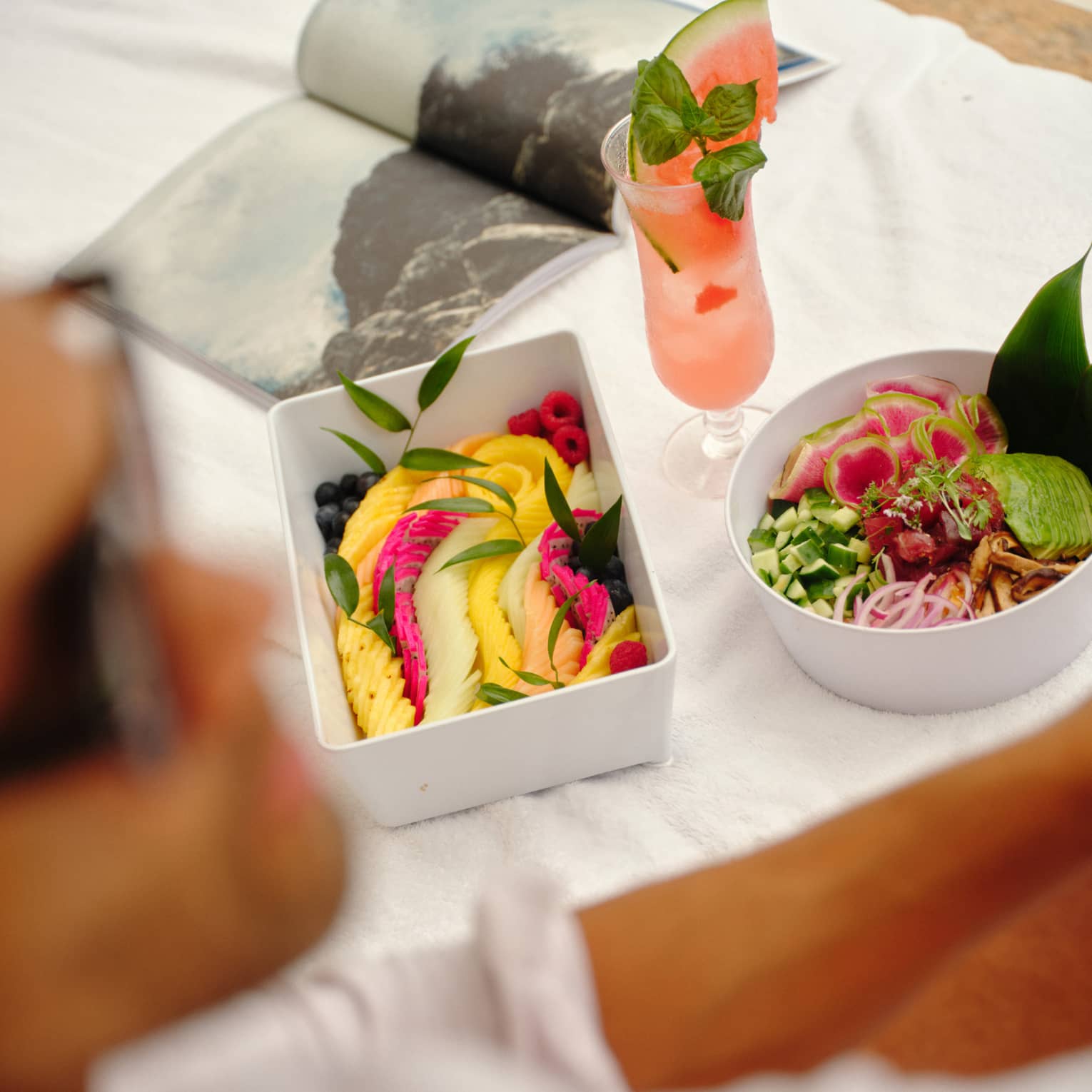 Fresh fruit and salad in white containers set on a day bed