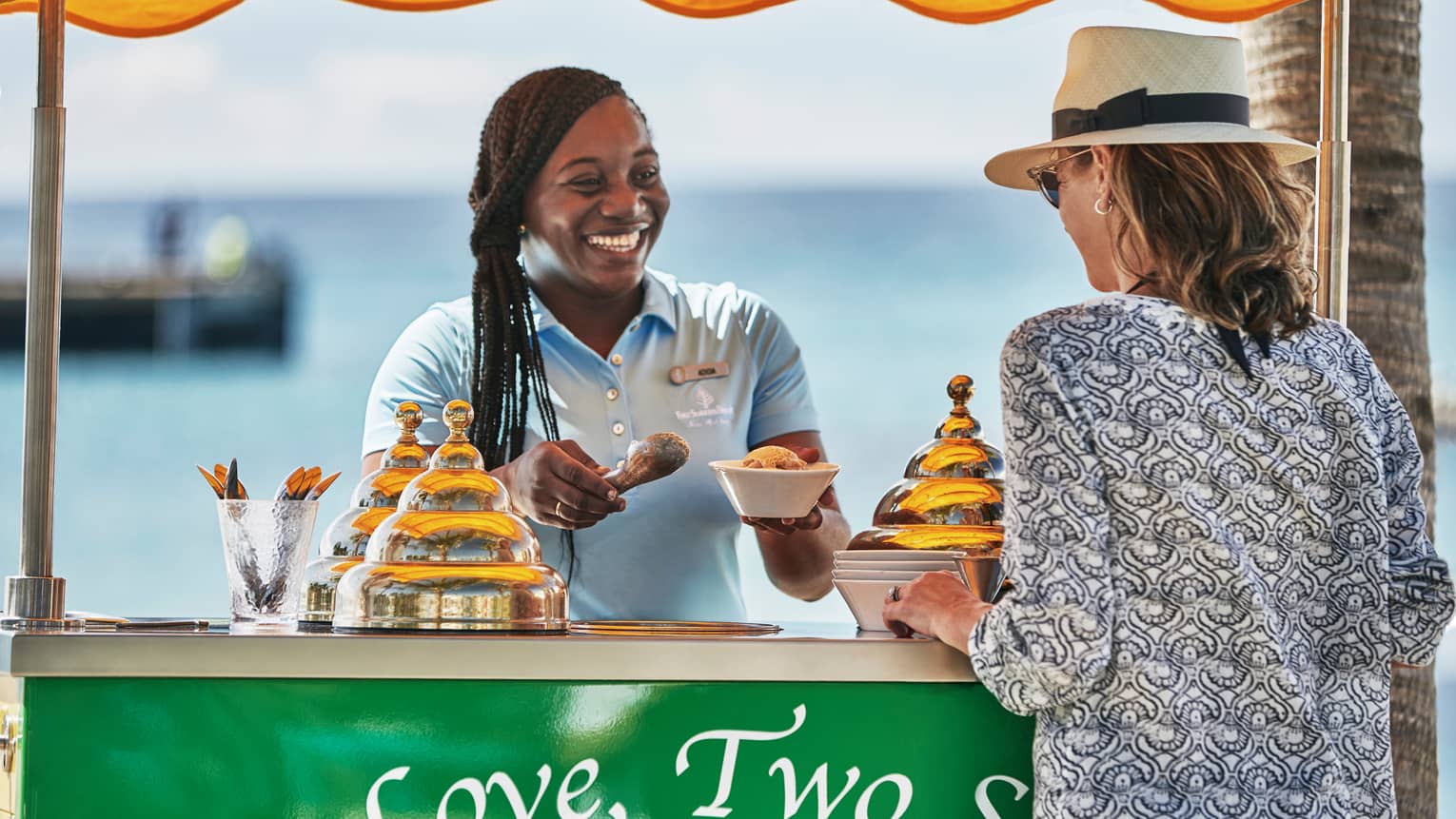 Smiling hotel staff scoops ice cream into dish for guest at beach stand