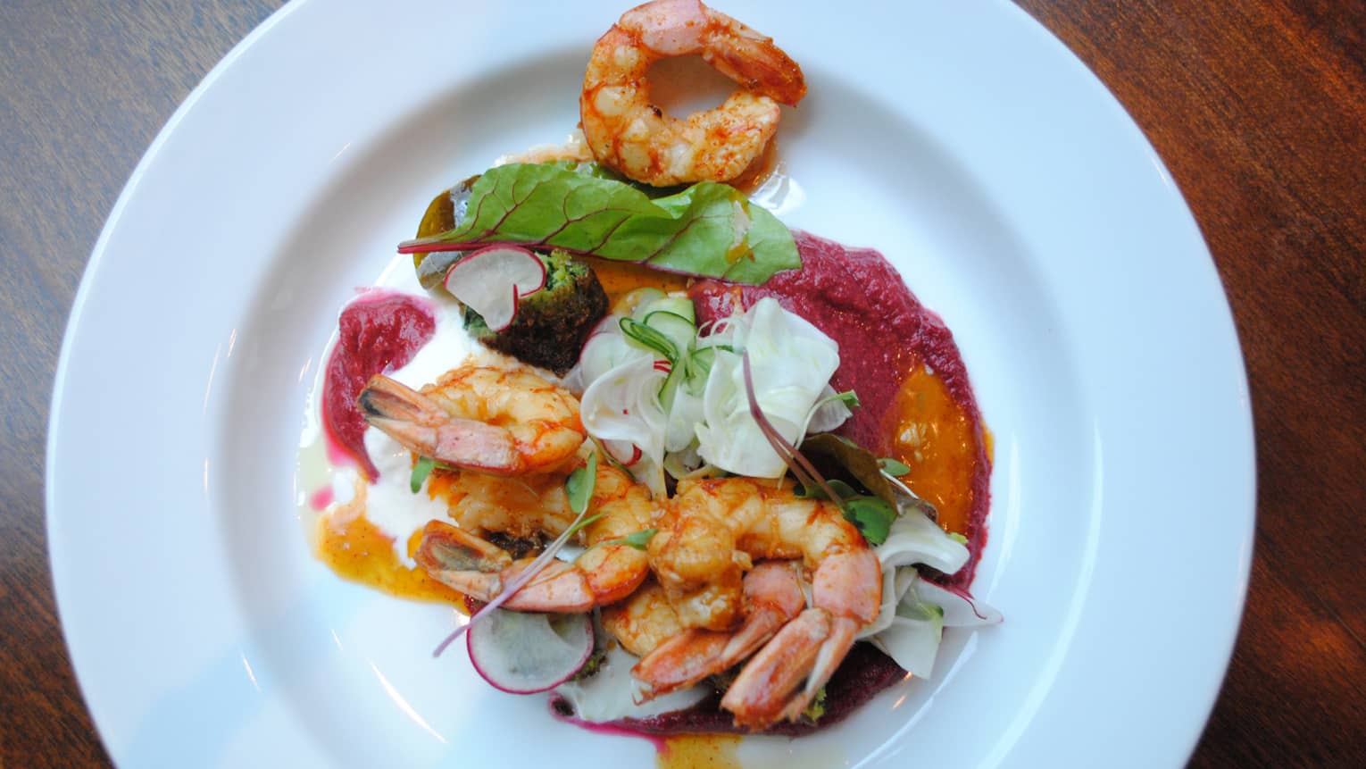 A shrimp dish is served with radishes, greens and a creamy sauce