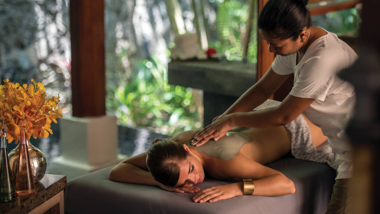 Masseuse rubs clay on woman's bare back, shoulders in spa