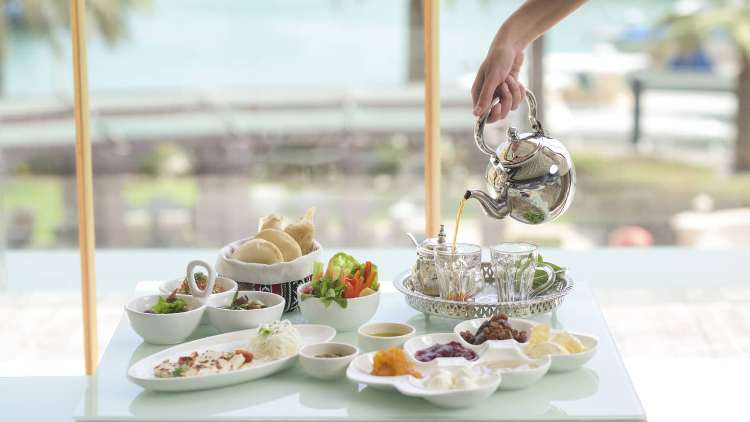 An assortment of small foods and dips near a pool, tea is being poured into a cup.