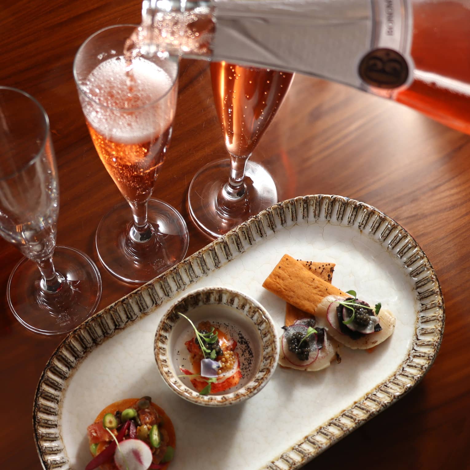 Champagne being poured into a glass beside a food dish