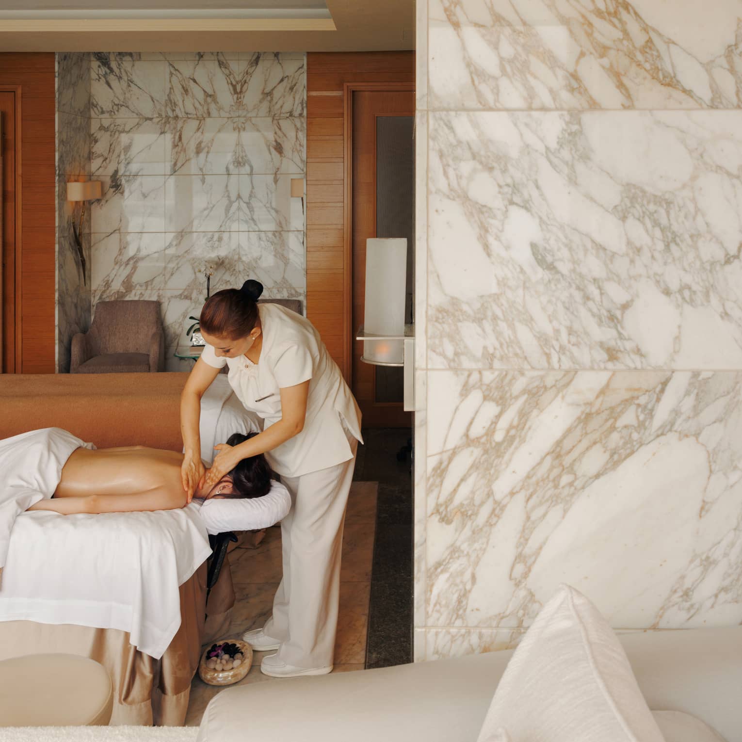 A female spa therapist performing a massage on a woman, face down on spa treatment table, in a chic luxury spa with marble walls