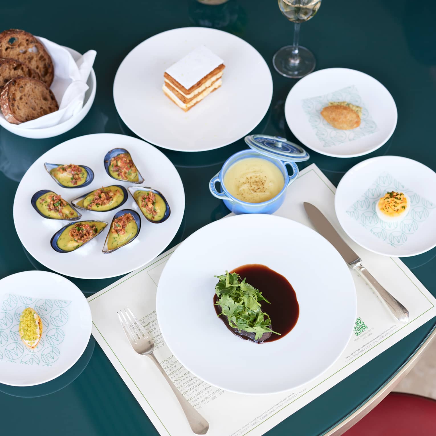 Tempting place setting with mixed greens-topped main course surrounded by sumptuous menu items, all on shiny white plates.