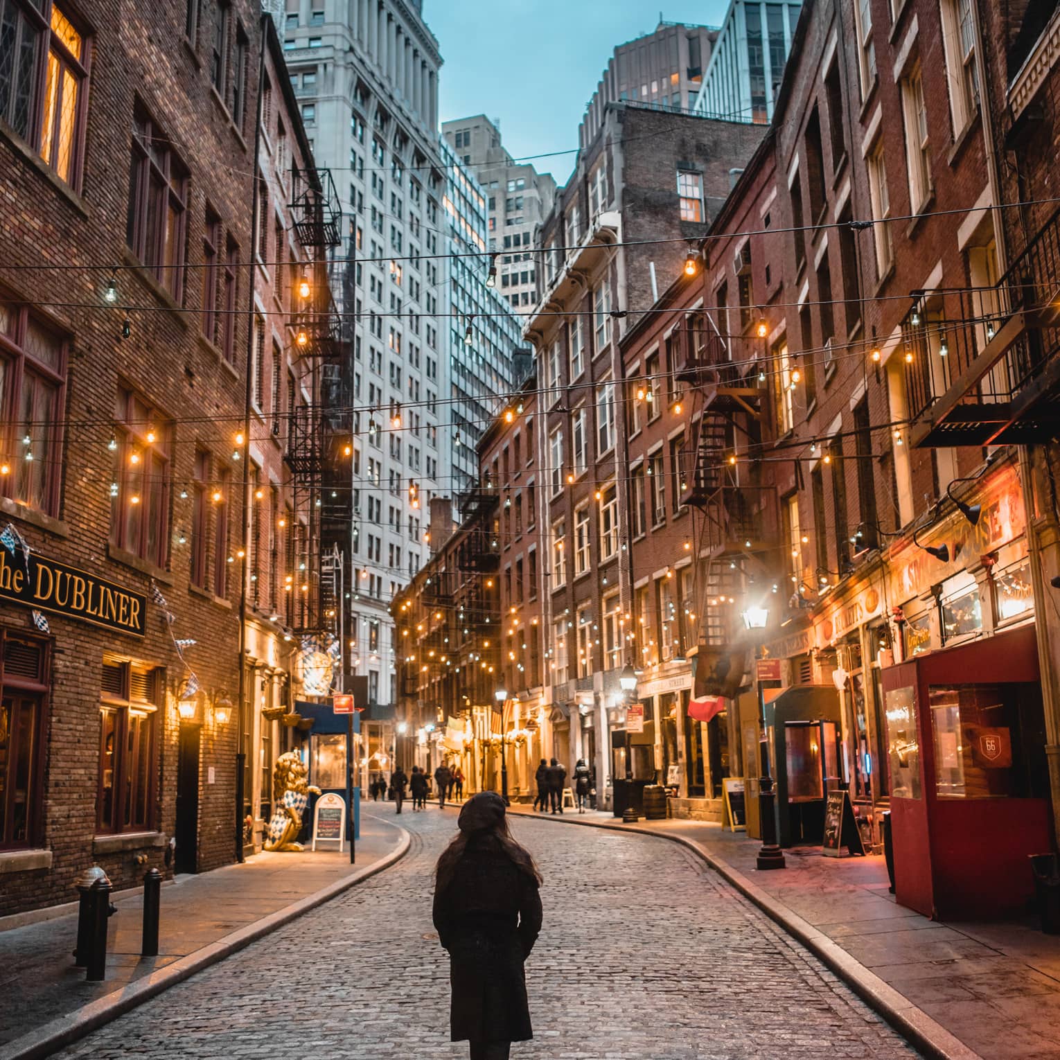 A woman in a winter coat walking down a street with many lights.