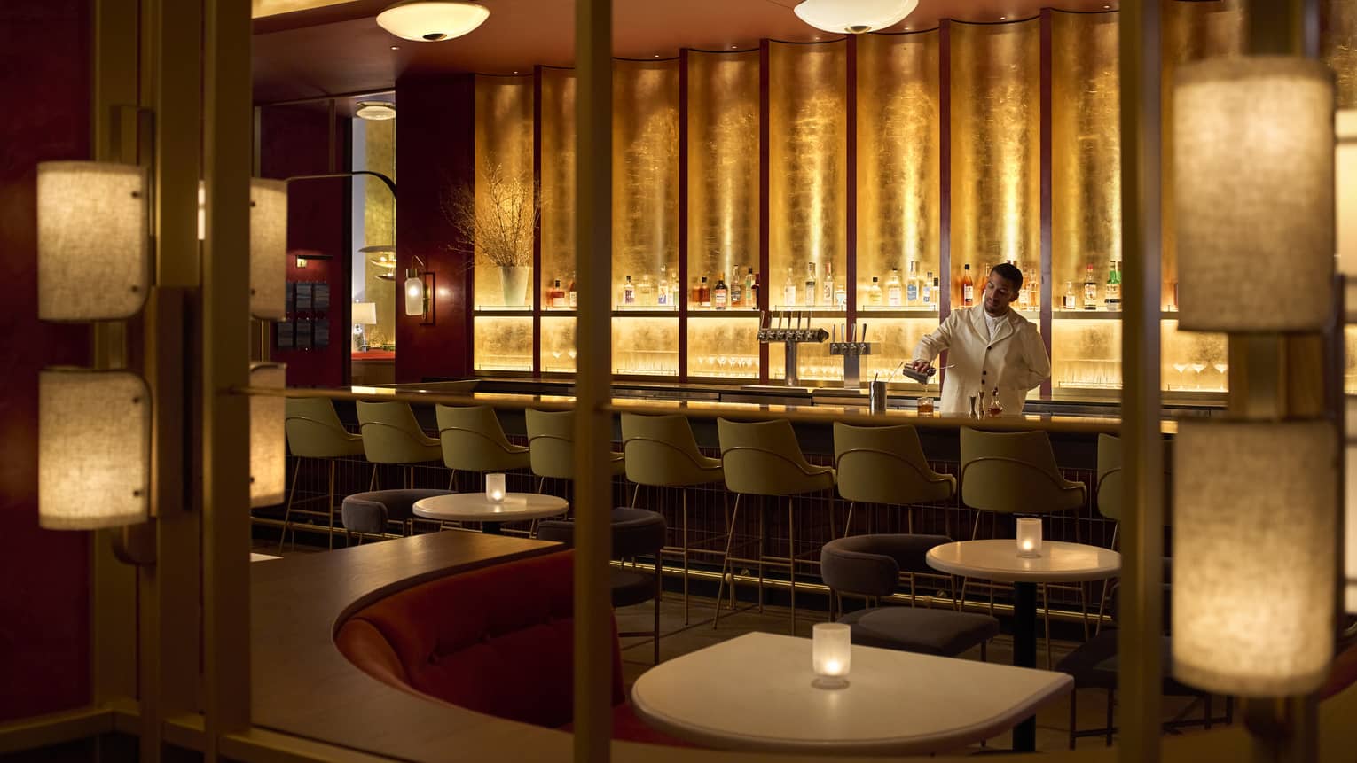 A bartender behind a bar area with warm lighting, small tables and chairs.