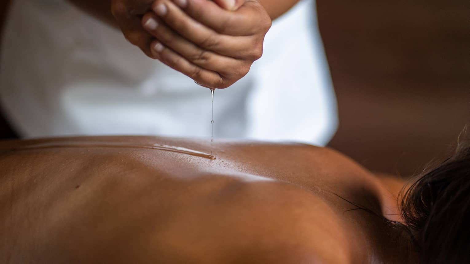 Delicate hands apply oil to a guest's back during a spa treatment