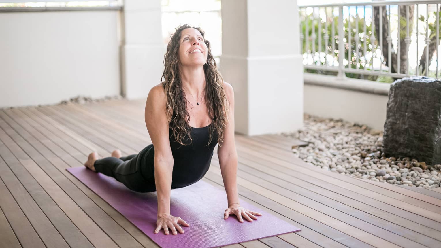 Woman smiles, looks up as she does yoga stretch on all fours on purple mat 