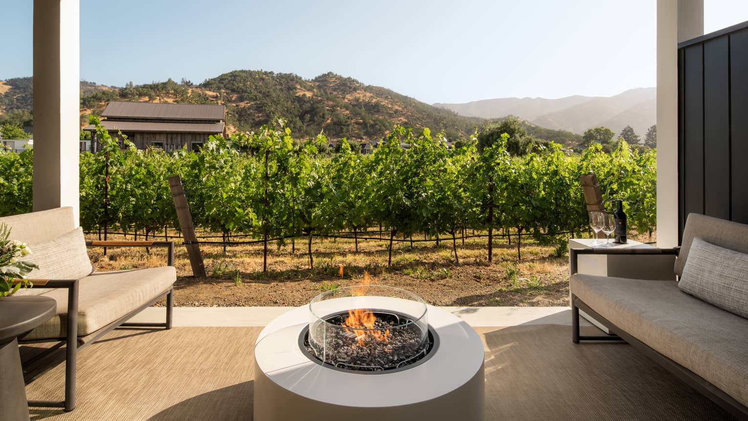 Covered patio featuring a gas fireplace in between two sofas, set next to lush vineyards