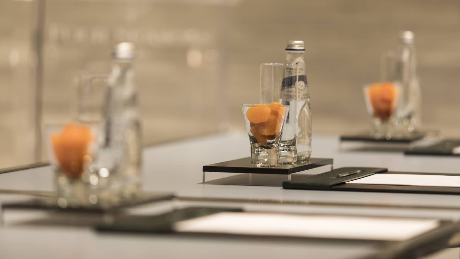 Close-up of meeting table place setting with agenda, dried apricots in glass, bottle of sparkling water