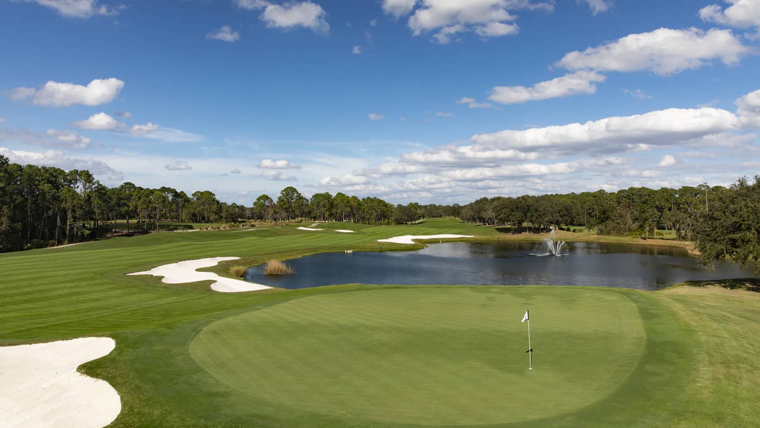 View across golf course green, small pond under blue sky 