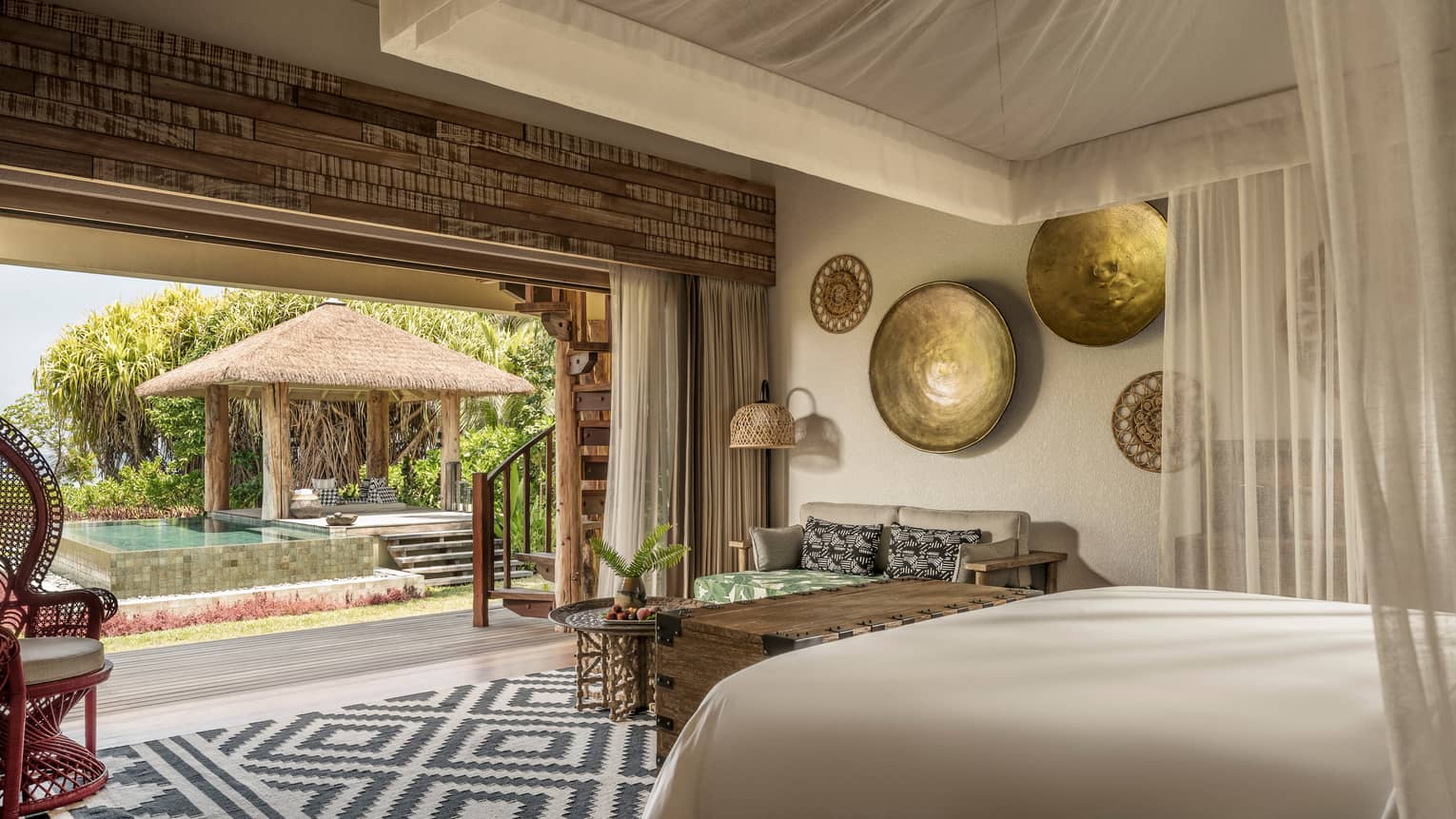 Luxury villa with canopy over bed, artwork on wall, rattan chair opens up to pool