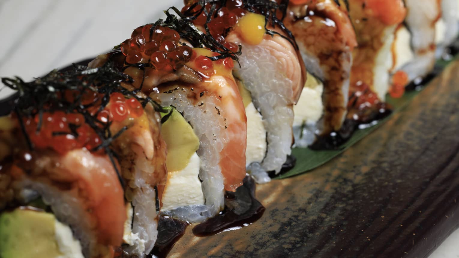 Close up of sushi roll with salmon, avocado, cream cheese, eel sauce, sesame and a pop of chili chutney.