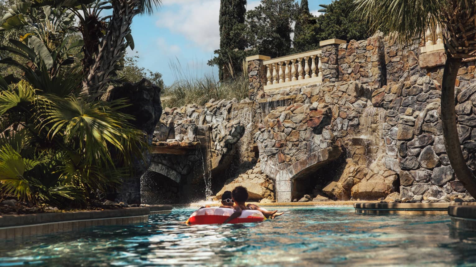 Guest in a float on the lazy river with palm trees on the side.