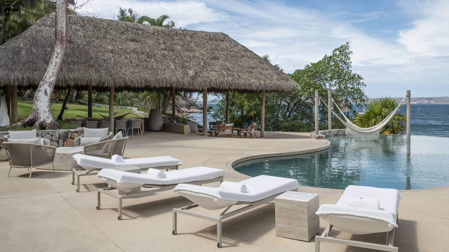 Private residence's pool terrace with four lounge chairs, dining area under a thatched-roof pavilion, and ocean views, at Four Seasons Resort Tamarindo