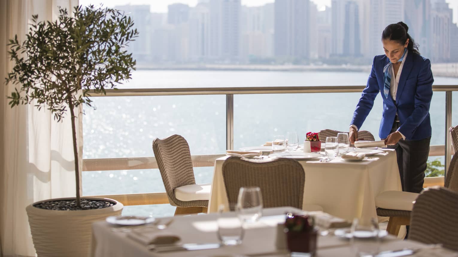 A four seasons staff setting an indoor  Cafe Milano table overlooking the water 