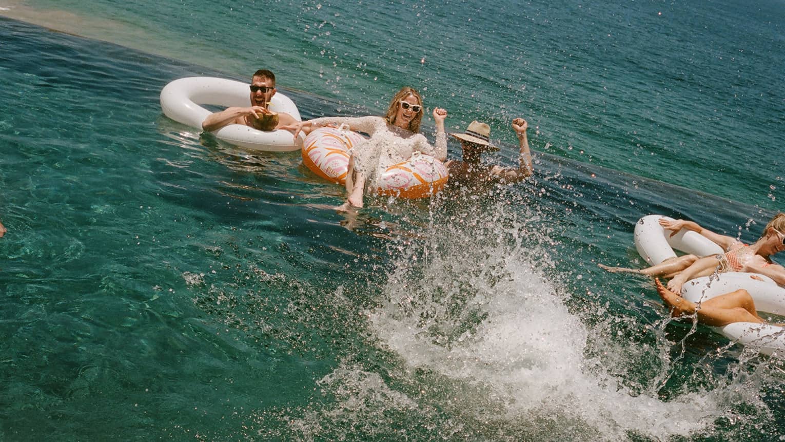 Several people floating and splashing in the ocean in inflatable tube floats