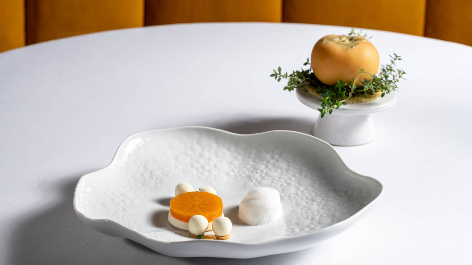 Lotus [Dry-Aged] Rakomelo Panna Cotta, Chamomile Lemon Thyme Cloud and Beeswax on scalloped round white dish 
