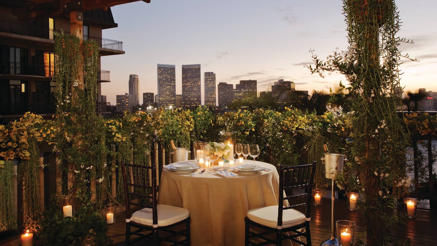 Round candle-lit dining table with wine, glasses in garden patio corner